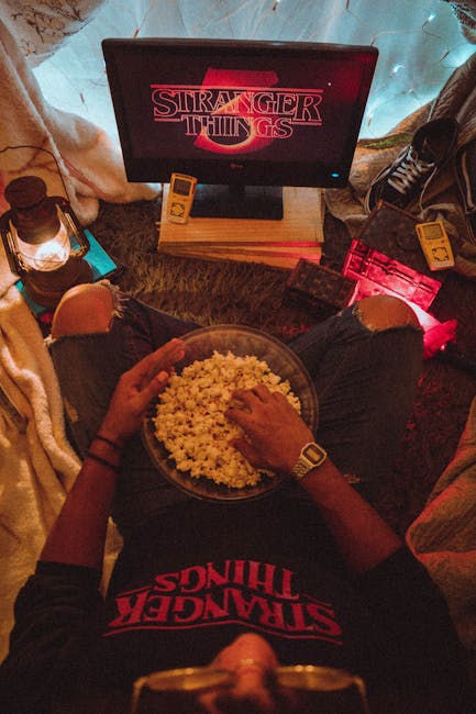 Person enjoying popcorn while watching Stranger Things in a cozy room setup.